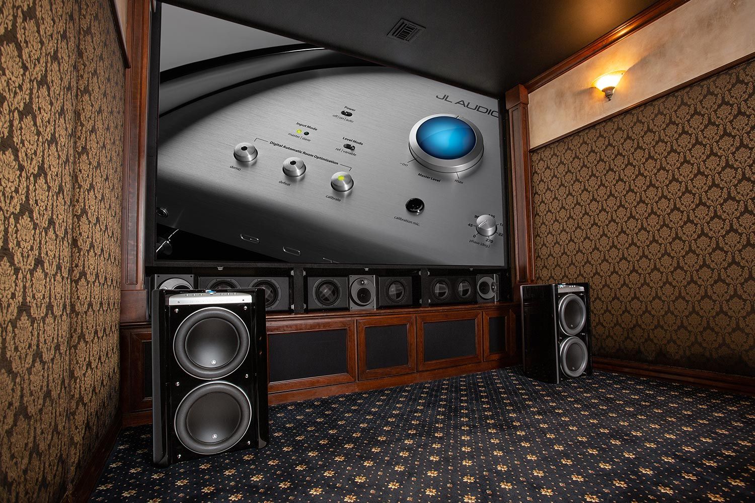 A dedicated home theater room with a large projection screen and intricate wall patterns. Gotham®v2 subwoofers are positioned prominently, providing powerful, compact bass that enriches the cinematic experience.